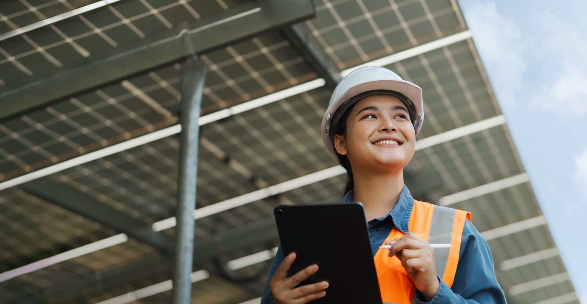 Female electrical engineer wearing hard hat using laptop checking solar panel farm equipment. Eco-friendly energy. Renewable clean energy technology concept.